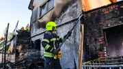 Ein Feuerwehrmann reißt eine Dachrinne an einem ausgebrannten Haus ab