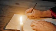Ein Mann schreibt bei Kerzenlicht.