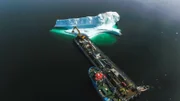 Ein Eisberg wird 'geerntet'. Der Bagger trägt große Brocken ab. Das reine Eisbergwasser ist begehrt für die Herstellung von Cidre, Bier und Wodka.