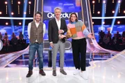 Moderator Jörg Pilawa (M.) mit den Kandidat:innen des Teams "Traumpaar": Dem Schauspieler Fritz Karl (l.) und der Schauspielerin Elena Uhlig (r.).