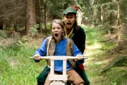 Konrad und der Jäger sind auf Konrads selbst gezimmertem Fahrrad, dem jegliche Bremse fehlt, auf dem Weg zu Großmutters Häuschen, um Rotkäppchen und Großmutter aus des Wolfes Bauch zu befreien.