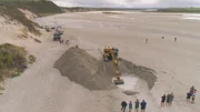 Ein Bagger gräbt ein Loch am Strand