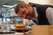 Dr. Mario Herger kostet einen veganen Chickenburger – die Rezeptur wurde entwickelt von einer künstlichen Intelligenz der Firma „NotCo“.