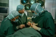 Prof. Brinkmann (Klausjürgen Wussow) und Udo (Sascha Hehn) bemühen sich um Dr. Vollmers (Christian Kohlund). (Darstellerin li. unbekannt).