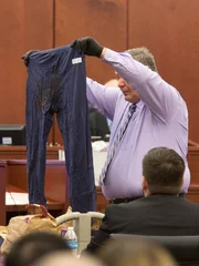 Das Verfahren gegen Shayna Hubers, die 2012 wegen Mordes an ihrem Freund verurteilt wurde, wird nach einem Problem mit einem Geschworenen neu aufgerollt. Der Polizeibeamte Dave Fornash aus Highland Heights zeigt die Hose, die Ryan Posten, 29, trug, als er von Shayna Hubers, 27, in seiner Wohnung in Highland Heights erschossen wurde. Fornash war am 12. Oktober 2012 der verantwortliche Beamte am Tatort. Hubers wurde im ersten Prozess des Mordes für schuldig befunden und zu 40 Jahren Gefängnis verurteilt, aber es wurde ihr eine Wiederaufnahme des Verfahrens gewährt, nachdem ihr Anwalt herausgefunden hatte, dass ein Geschworener im ersten Prozess bereits wegen eines Verbrechens verurteilt worden war. Den Vorsitz hat Campbell County Richter Daniel Zalla inne.