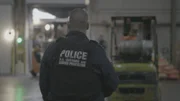 Officer stands by while workers move shipment at warehouse facility. (National Geographic)