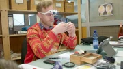 Ep6 - Axel inspecting a gold chain with a pendant.