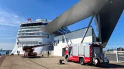 A firetruck at the cruise ship terminal Warnemünde. The turntable fire escape is extended to a window of the terminal. Behind the terminal lies a cruise ship.