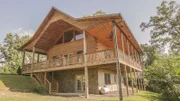 The exterior of the Deep Creek Cabin shows a large wrap-around deck and detailed woodwork, as seen on Log Cabin Living.