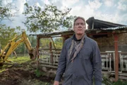 Chris medium close up with damaged house and excavator in the background.