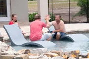 JB Holmes and Lucas Congdon high five and relax on loungers in pool, Erica and Baby Holmes watch from pool ledge.