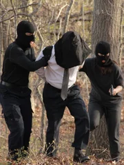 Eco-terrorists lead a hooded Sidney through the woods at gun point