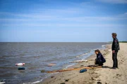 Polizistin Süher Özlügül (Sophie Dal) kniet vor den Überresten eines Segelbootes am Strand, während ihr Kollege Henk Cassens (Maxim Mehmet) aufs offene Meer blickt. Was hat sich hier nur ereignet?
