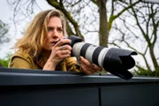 Journalistin Anna Mansholt (Marie Burchard) späht neugierig über eine Mauer. Exklusive Fotos würden ihr die Titelseiten sichern.