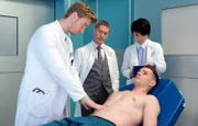Seit Dr. Kaminski (Udo Schenk, mi.) weiß, dass Florian Klein (Aaron Koszuta, li.) möglicherweise ein Hochstapler sein könnte, hat er ein besonderes Auge auf ihn. Allerdings wäre es schade, da Florian ein brillanter Diagnostiker werden könnte. Dies stellt er auch bei der Untersuchung von Georg Fichte (Maximilian Pekrul, liegend) wieder unter Beweis. re.: PJlerin Chen Mi Lan (Yun Huang)