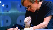 Dr. Sid Hammerback (Robert Joy) untersucht die Leiche des Börsenmaklers Jim Morris (Brian Catalano). Jemand hat ihm Isolierschaum in den Mund gespritzt, woraufhin er kläglich erstickte.
