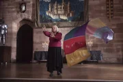 Ada Graustein (Clare Higgins), die Direktorin der Hexenakademie, trägt gerade ein Duell gegen ihre Zwillingsschwester aus. Dabei sieht sie den fliegenden Wandbehang nicht auf sich zukommen.