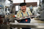 Sebastian Lege steht in seiner Werkstatt und hält ein Tablett mit Schokoriegeln in die Kamera.