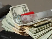 Crystal meth pipe and lighter placed on top of pile of cash.