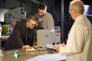 Actor portraying Greg Phillips and a technician use a high-powered microscope to look inside the servo valve for minuscule scratches