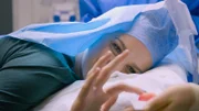 Close up shot of Charnelle M lying on treatment bed, touching the cyst that has just been removed from her neck.