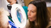 CU shot of Dr Emma looking through the magnifying glass to examine Kate's face