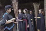 Mildred (Bella Ramsey, M.) kann es kaum fassen: Frau Drill (Shauna Shim) möchte, dass sie als Anführerin bei der Besenflugschau fliegen soll. Die Freundinnen Felicitas, Edith und Maude (v. l. n. r.: Dagny Rollins, Tamara Smart, Meibh Campbell) sind auch erstaunt.