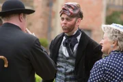 Sid Carter (Alex Price, M.) erlaubt sich einen Spaß mit Mrs McCarthy (Sorcha Cusack, r.) und Father Brown (Mark Williams, l.) am Filmset. Er bedient sich unbemerkt an den Requisiten der Filmcrew.