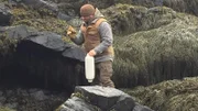 Bill McConnell on a rocky shore with a buoy and work gloves on Maine.