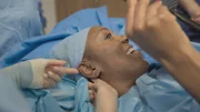 Close up of Samantha on clinic bed post surgery looking in mirror and smiling. Ep3.