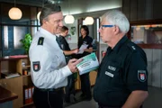 Haller (Hannes Hellmann, l.) will mit allen Kollegen ein Mitarbeitergespräch führen. Wolle (Harald Maack, r.) wird der Erste sein. Doch warum drückt ihm Haller im gleichen Atemzug eine Broschüre zur „Vorbereitung auf den Ruhestand“ in die Hand?