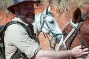 Gavin LInsell stroking a horse at a lake in the Bahia wilderness.