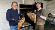 Spitzenkoch Björn Freitag (l.) und Fischwirt Philipp Stobbe (r.) holen den heißgeräucherten Lachs aus dem Räucherofen.
