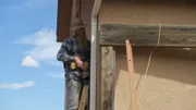 Russ steigt auf eine Leiter und bereitet sich auf das Bohren von Pfosten vor