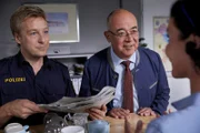 Polizist Mohr (Max Müller, l.) und Achtziger (Alexander Duda, M.) sehen in der Tageszeitung ein Foto von Stockl (Marisa Burger, r.) , die erfolgreich einen Sponsor für die Musikakademie geworben hat.
