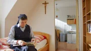 Schwester Maria blättert auf ihrem Bett sitzend in einem Fotoalbum.