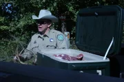 Warden Zak Benge holding deer antlers next to truck with an open cooler of meat.