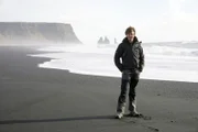 Presenter Brian Cox auf Island. An der Küste treffen Wasser und Felsen aufeinander so wie auf Objekten im äußeren Sonnensystem. Wasser befindet sich allerdings nur auf der Erde in seinem flüssigen Aggregatszustand.