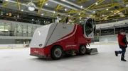 Volker, der Eismeister, fährt mit der Eismaschine über die Eislaufbahn und macht das Eis schön glatt.