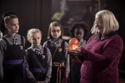 Die Direktorin Frau Graustein (Clare Higgins) ist zufrieden: Der Grundstein ist wieder da - gerade noch rechtzeitig! Esther (Jenny Richardson, l.) ihre Schwester Sybille und deren Freundinnen Clarissa und Beatrix (v.l.n.r.: Trixie Hyde, Kitty Slack, Ynez Williams) sind auch froh, dass der Stein nun endlich wiedergefunden wurde.