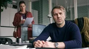 Jochen Mohn (Stefan Rudolf) sitzt gedankenverloren an seinem Schreibtisch. Hinten: Kriminalhauptkommissarin Hermine Grill (Xenia Tilling).
