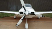 The front of a white plane sitting by a hangar.