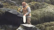 Bill McConnell on a rocky shore with a buoy and work gloves on Maine.