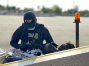 Ein CBP-Beamter inspiziert ein Gepäckstück, das aus einem Flugzeug kommt.