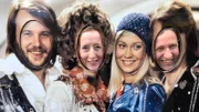 Entertainerin Kiona und Kreuzfahrtdirektor Jöhrn Hofer beim Besuch des ABBA-Museums, wo sie ihre Köpfe durch ein ABBA Plakat stecken.