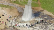 Die sprudelnden Geysire sind eine der Hauptattraktionen für Inselbesucher. Eine Wasserfontäne schießt in die Luft, drumherum stehen Menschen.