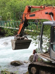 Weite Aufnahme von Bagger und Transportkiste, getrennt durch einen Fluss.