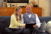 Franzi (Mia Löffler, KLD) sitzt mit ihrem Vater Hubert (Bernhard Ulrich) auf der Couch und zeigt ihm ein Spiel auf dem Tablet.