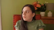 Medium shot of Natalia wearing a green shirt from intv. Sitting in red chair, looking to her right