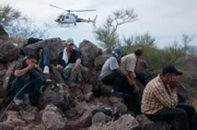 Nogales, AZ: Handcuffed men sitting on rocks, with a helicopter hovering in the background. Illegal immigrants and smugglers can be located with the use of helicopters.